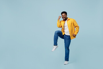 Full body excited young man of African American ethnicity 20s wear yellow shirt doing winner gesture celebrate clenching fists say yes isolated on plain pastel light blue background studio portrait