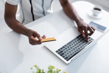 cropped view of senior african american man holding credit card near laptop while shopping online.