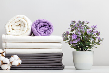 Stack of bed linen, sheets and towels with cotton branch and potted plant on table