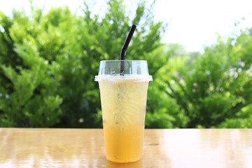 Iced fresh drink honey lemon soda refreshment juice in the glass put on wood table and green tree background