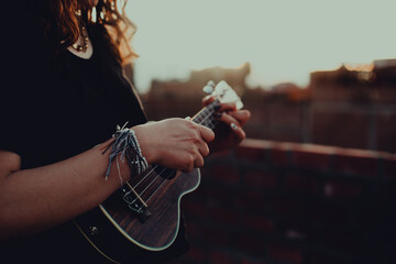 Mujer tocando ukulele en un techo con el atardecer detrás. Concepto de musica.