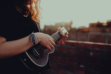 Mujer tocando ukulele en un techo con el atardecer detrás. Concepto de musica.