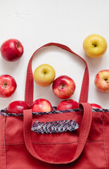 Red eco bag with red and golden apples. Fabric shopper with apples on a white background. Eco friendly shopping, Zero waste. Vegan concept. Reusable mesh. Sustainable lifestyle.
