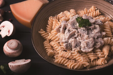 Fusilli pasta, with champignons in cream sauce, top view, with ingredients, on a wooden table, no people,