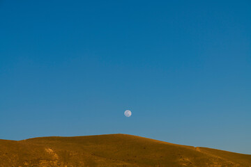 Beautiful full moon over the hill on the blue sky.