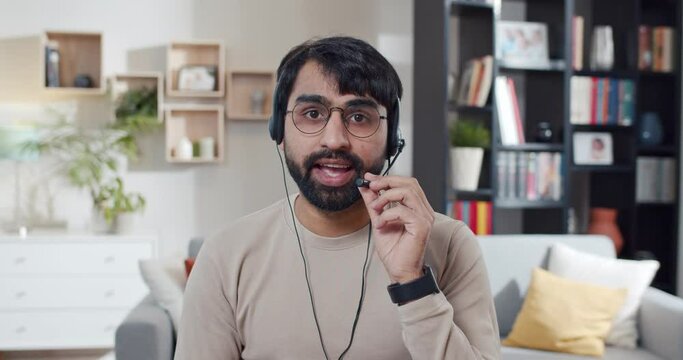Portrait of Arabian young man in glasses and headset talking to camera and explaining something. At home. Arab male blogger videochatting or making new video for blog. Videoblogger. Video bloging.
