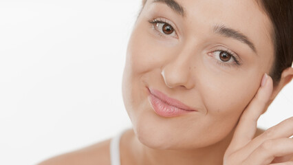 Obraz premium Extreme clos-up of young gorgeous Caucasian woman touches her face smiling for the camera on white background | Smooth skin and face care concept