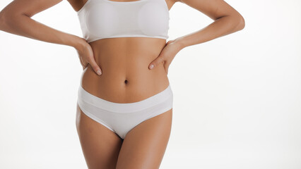 Naklejka na ściany i meble Medium shot of fit African American woman in white underwear puts her hands on her waistline on white background | Body care concept