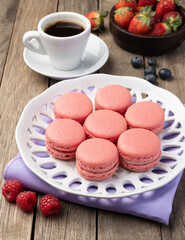 Fototapeta na wymiar Berry macarons on a plate with coffee over wooden table