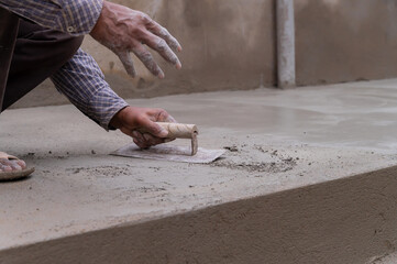 Indian labour levelling plastered floor using flat trowel and cement manually, Stock image.