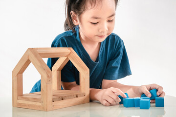Little girl playing with blue toy blocks and wooden house. A happy kid has concentred to creates constructions with wood bricks. Nursery and childhood educational game for baby and toddler concept