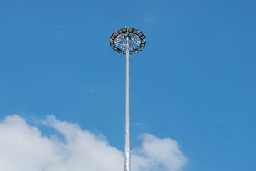 Tall steel mast with powerful searchlights against the sky.