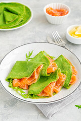 Green spinach crepes or pancakes with smoked salmon and soft cheese on a plate on the gray background. Copy space.