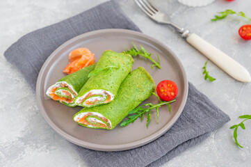 Green spinach crepes or pancakes with smoked salmon and soft cheese on a plate on the gray background. Copy space.