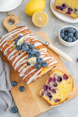 Lemon blueberry cake with lemon icing and fresh berries on top on the board on a gray concrete background with cup of tea. Selective focus. Copy space.