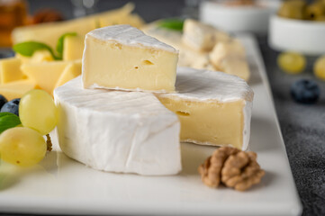 Cheese plate with a variety of cheeses, honey, grapes, nuts, olives, blueberries and fresh herbs on a concrete background. A festive snack.