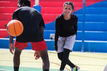 Fototapeta premium Young woman with afro hair playing basketball against men