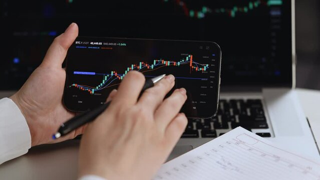 Stock market trader analyzing bitcoin price trend. Investment stockbroker stock market analysis data graph with price rates. Trading bitcoin crypto currency using laptop and smartphone.