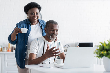 senior african american man gesturing near wife while looking at laptop during video chat.