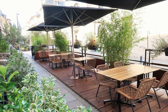 Tables, chaises, parasols et plantes vertes sur la terrasse &eacute;ph&eacute;m&egrave;re v&eacute;g&eacute;talis&eacute;e (terrasse estivale / extension de terrasse / contre-terrasse) d'un restaurant / caf&eacute; / bar (France)