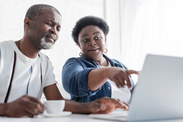 retired african american woman pointing at laptop near husband.