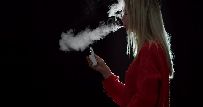 Vaping young woman on black background