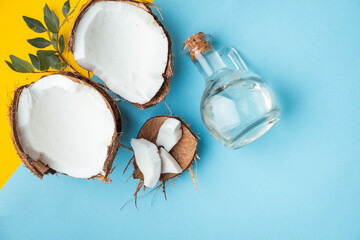 Cracked coconut with coconut oil in glass bottle on the yellow and blue background