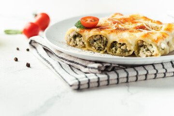 Cannelloni Italian pasta filled with meat and spinach, covered with cheese on the white background