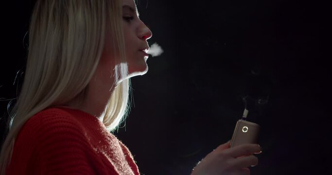 Vaping young woman on black background