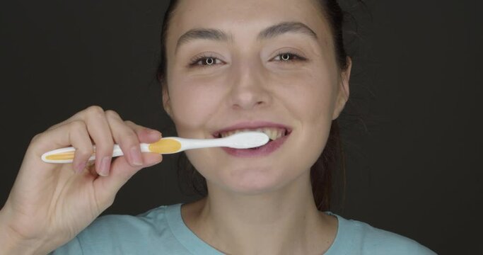 Happy young woman brushing teeth with activated charcoal tooth paste on dark background