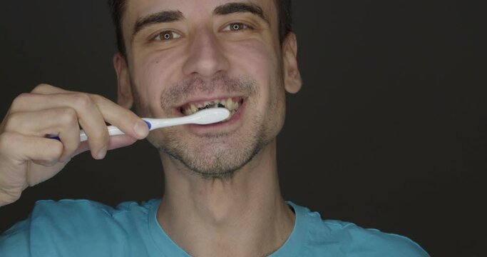 Happy young man brushing teeth with activated charcoal tooth paste on dark background