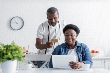 senior african american man holding credit card while online shopping with happy wife.