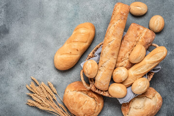 Assorted fresh bread in a basket on a gray concrete background. Top view, selective focus.
