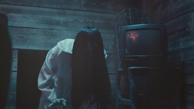 Scary Ghost Woman Crawling or Walking In Horror Halloween Scene . Droning television inside dark empty room . Little girl in white sundress . The ring movie theme . Girl with long black hair. Close up