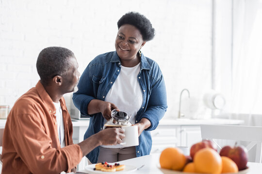 happy african american wife serving coffee to smiling husband during breakfast.