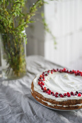 A delicious carrot cake stands on the table, garnished with white mascarpone cream and cranberries. A beautiful dessert for every day. There are greens in a vase on the table. Spring still life