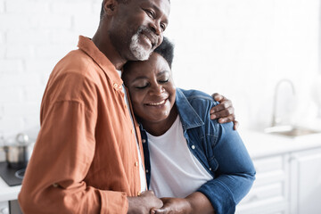 happy and senior african american couple holding hands and hugging at home.