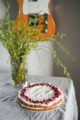 A delicious carrot cake stands on the table, garnished with white mascarpone cream and cranberries. A beautiful dessert for every day. There are greens in a vase on the table. Spring still life