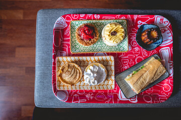 Delicious home breakfast, with red tray with colorful plates with apple pie, lemon pie, strawberries 'kuchen' cake, passion fruit cheese cake, gourmet sandwich and vanilla cake