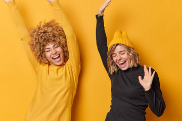 Happy teen girls dance carefree keep arms raised up feel energetic dressed in casual turtlenecks...