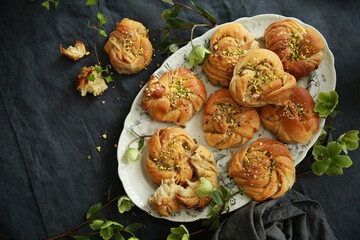 Bakery products. Buns with pistachios, nuts on a platter on a gray tablecloth on a table with flowers and branches with green leaves. Homemade, summer kitchen. Background image, copy space