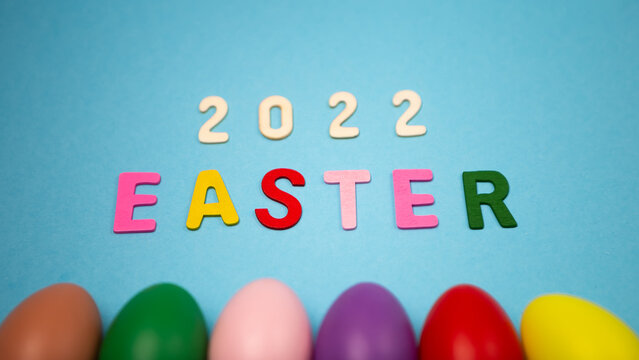 Flat lay lined up set of decorated hand painted chaotically scattered colorful eggs on blue background. Happy Easter 2022 concept composition. Image with copy free space for text message
