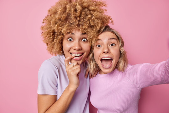 Cheerful Young Woman Feel Amazed And Full Of Happiness Pose For Making Selfie Stand Next To Each Other Dressed Casually Isolated Over Pink Background. Self Portrait Of Cheerful Female Friends