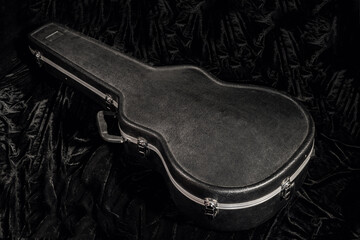 Black hard case for guitar lying on black velor fabric. Closed cover for a stringed musical instrument close up. Black wardrobe trunk for acoustic guitar.