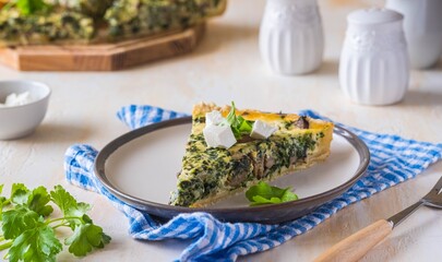 Unsweetened sliced open pie, shortcrust pastry quiche stuffed with spinach, champignons and cheese on a ceramic plate on a light concrete background. Unsweetened pastry recipes.