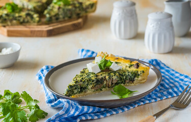 Unsweetened sliced open pie, shortcrust pastry quiche stuffed with spinach, champignons and cheese on a ceramic plate on a light concrete background. Unsweetened pastry recipes.