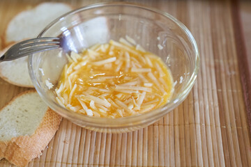 Close-up of mixed eggs in a transparent glass bowl with grated cheese. Step-by-step cooking of eggs for breakfast