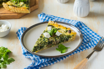 Unsweetened sliced open pie, shortcrust pastry quiche stuffed with spinach, champignons and cheese on a ceramic plate on a light concrete background. Unsweetened pastry recipes.