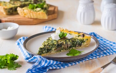 Unsweetened sliced open pie, shortcrust pastry quiche stuffed with spinach, champignons and cheese on a ceramic plate on a light concrete background. Unsweetened pastry recipes.