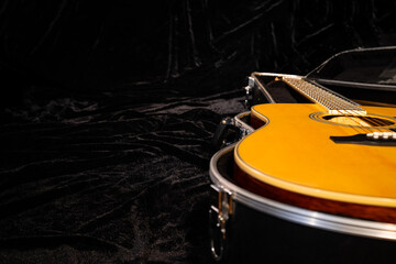 Black hard case with a wooden yellow acoustic guitar lying on a black velor fabric. Close up of an...